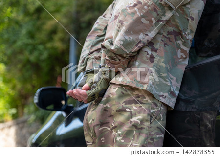 Military man after detention holds his hands cuffed behind his back while standing next to a car. Military man after detention holds his hands cuffed behind his back while standing next to a car. 142878355