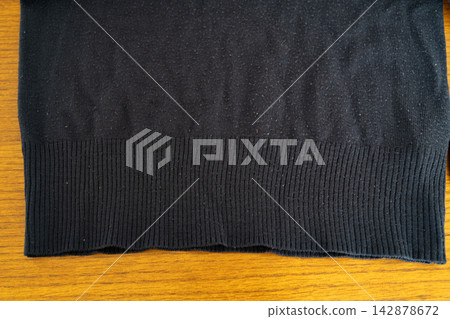 Photo of the ribbed detail at the hem of a black knit sweater. 142878672