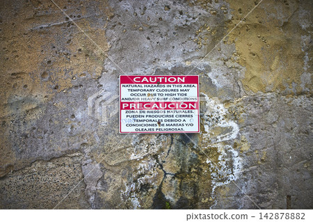 Caution Sign on Weathered Wall Warning of Natural Hazards Near Beach Access Caution Sign on Weathered Wall Warning of Natural Hazards Near Beach Access 142878882