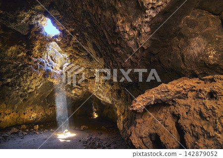 Lava Tube Sunbeam Illuminating Rugged Cave Interior with Volcanic Rock Formations 142879052