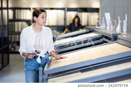 in store,female buyer carefully examines laminate sample. Woman chooses flooring material 142879739