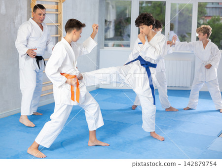 Teenagers in kimonos working on kicks in pairs during group training Teenagers in kimonos working on kicks in pairs during group training 142879754
