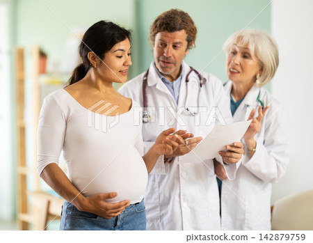 Happy pregnant woman discussing medical test results with two doctors Happy pregnant woman discussing medical test results with two doctors 142879759