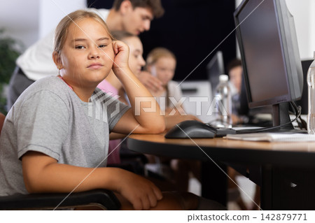 Confused preteen girl sitting at computer table in training room Confused preteen girl sitting at computer table in training room 142879771