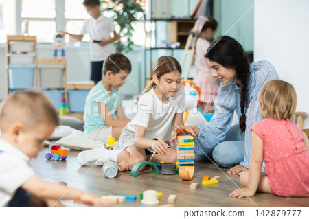 Children of different ages playing with wooden blocks with teacher Children of different ages playing with wooden blocks with teacher 142879777
