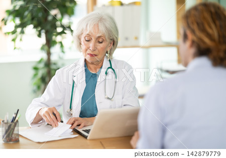 At clinic, man is at doctors appointment, talking at table At clinic, man is at doctors appointment, talking at table 142879779