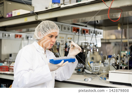 Female chemist working in laboratory, analyzing liquid samples in test flasks Female chemist working in laboratory, analyzing liquid samples in test flasks 142879808