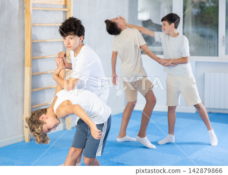 Diligent preteen student twisting his opponent's arm in sports hall Diligent preteen student twisting his opponent's arm in sports hall 142879866
