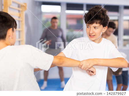 Focused kids in pair exercising self-defense movements during group class in sports studio, closeup Focused kids in pair exercising self-defense movements during group class in sports studio, closeup 142879927