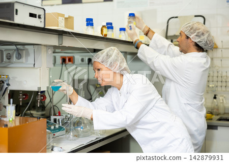 Team of chemists working in research laboratory performing experiments on lab equipment Team of chemists working in research laboratory performing experiments on lab equipment 142879931