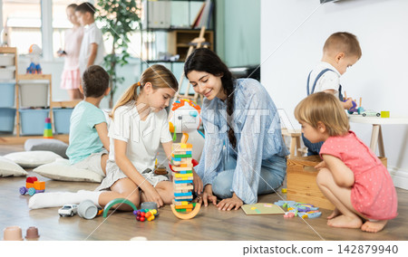 Children playing with toys with teacher nearby in kindergarten Children playing with toys with teacher nearby in kindergarten 142879940