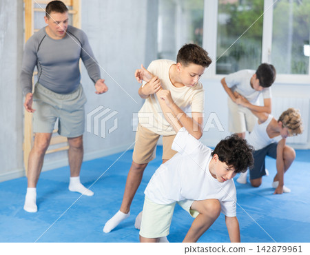 Diligent preteen student twisting his opponent's arm in sports hall Diligent preteen student twisting his opponent's arm in sports hall 142879961