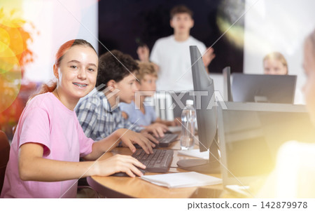 Portrait of teen schoolgirl sitting at table in computer class during lesson, smiling at camera. Concept of teenagers and technologies Portrait of teen schoolgirl sitting at table in computer class during lesson, smiling at camera. Concept of teenagers and technologies 142879978