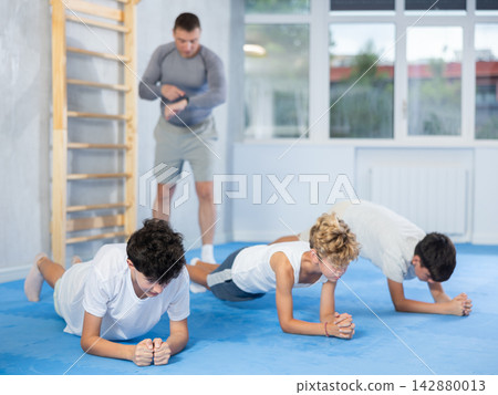 Portrait of kids doing plank, bench press, exercising together with male trainer in gym Portrait of kids doing plank, bench press, exercising together with male trainer in gym 142880013