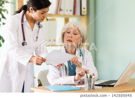 Two female doctors checking medical records on laptop Two female doctors checking medical records on laptop 142880048
