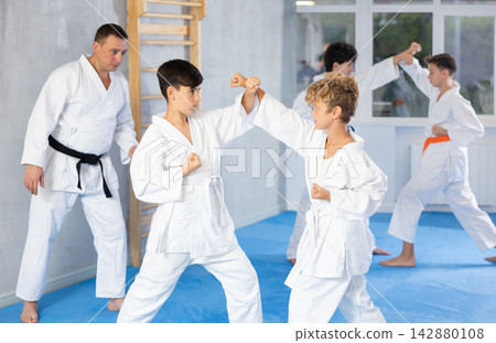 Teenagers in kimonos working on hand strikes in pairs during group training Teenagers in kimonos working on hand strikes in pairs during group training 142880108