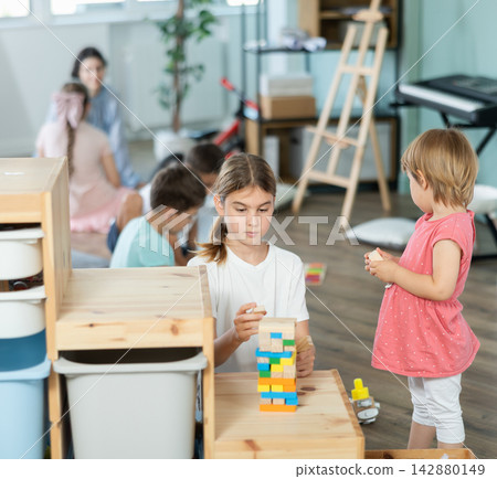 Toddler and schoolgirl building colorful tower together on wooden furniture Toddler and schoolgirl building colorful tower together on wooden furniture 142880149