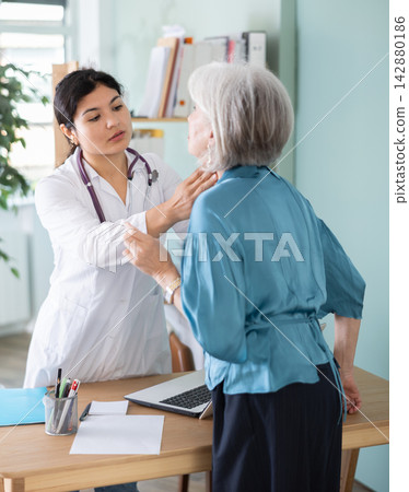 Senior woman holds sore spot one sore throat at doctors appointment Senior woman holds sore spot one sore throat at doctors appointment 142880186