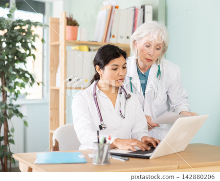 Senior and adult female doctors bent over laptop, work with medical soft Senior and adult female doctors bent over laptop, work with medical soft 142880206