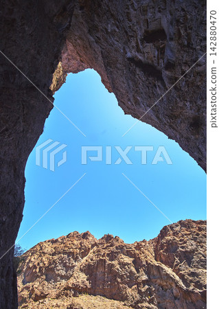 Cave Opening with Sunlit Desert Cliffs and Blue Sky in Rugged Arizona Landscape Cave Opening with Sunlit Desert Cliffs and Blue Sky in Rugged Arizona Landscape 142880470