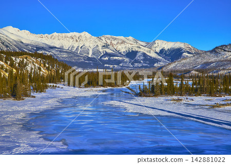 Frozen River and Pine Forest with Snowy Mountains Under Blue Sky Winter Frozen River and Pine Forest with Snowy Mountains Under Blue Sky Winter 142881022