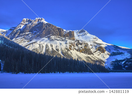 Snow Covered Mountain Forest and Frozen Lake in Winter Light Snow Covered Mountain Forest and Frozen Lake in Winter Light 142881119