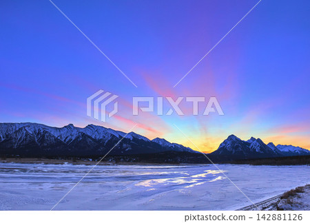 Panoramic Winter Sunrise Over Snowy Mountains and Frozen Lake in Alberta 142881126