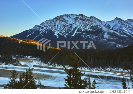 Snow Covered Mountain River and Evergreen Forest at Sunrise in Winter Snow Covered Mountain River and Evergreen Forest at Sunrise in Winter 142881144