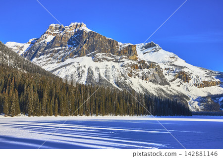Snow Covered Mountain Forest and Frozen Lake Under Clear Blue Winter Sky Snow Covered Mountain Forest and Frozen Lake Under Clear Blue Winter Sky 142881146