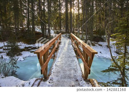 Winter Bridge Over Frozen River With Sunburst In Forest Trail Winter Bridge Over Frozen River With Sunburst In Forest Trail 142881168