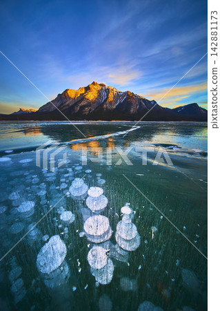 Frozen Methane Bubbles and Snowcapped Mountains Reflected on Winter Lake Surface 142881173