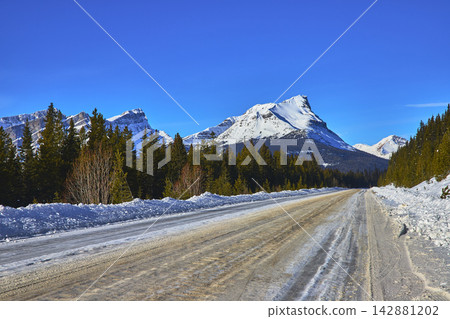 Winter Highway Through Snowy Mountains And Evergreen Forest In Banff Alberta Winter Highway Through Snowy Mountains And Evergreen Forest In Banff Alberta 142881202