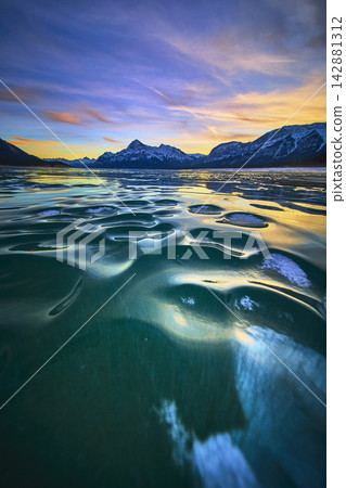 Frozen Lake Ice Patterns at Sunset with Dramatic Mountain Skyline Winter Landscape Frozen Lake Ice Patterns at Sunset with Dramatic Mountain Skyline Winter Landscape 142881312