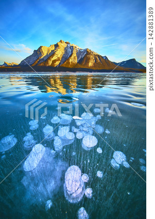 Frozen Methane Bubbles Under Ice with Snowy Mountain and Blue Winter Sky Frozen Methane Bubbles Under Ice with Snowy Mountain and Blue Winter Sky 142881389