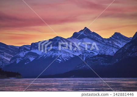 Winter Sunset Over Frozen Lake and Snowy Mountain Peaks with Vibrant Sky Winter Sunset Over Frozen Lake and Snowy Mountain Peaks with Vibrant Sky 142881446