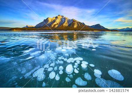 Frozen Lake with Methane Bubbles and Snow Covered Mountain Range in Winter Frozen Lake with Methane Bubbles and Snow Covered Mountain Range in Winter 142881574