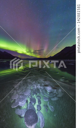 Winter Northern Lights Over Frozen Lake With Methane Bubbles And Mountain Silhouettes Winter Northern Lights Over Frozen Lake With Methane Bubbles And Mountain Silhouettes 142881581