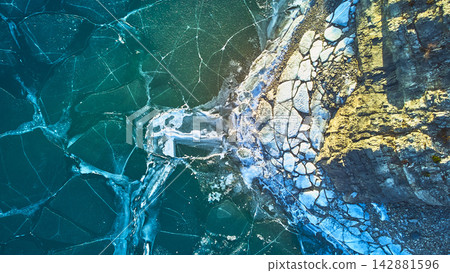 Aerial Frozen Lake Cracked Ice Patterns and Rocky Shoreline Winter Top Down Aerial Frozen Lake Cracked Ice Patterns and Rocky Shoreline Winter Top Down 142881596