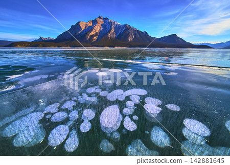Frozen Lake Ice Bubbles and Snowy Mountain Reflections in Winter Landscape Frozen Lake Ice Bubbles and Snowy Mountain Reflections in Winter Landscape 142881645
