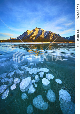 Frozen Lake Methane Bubbles and Snowy Mountains Under Blue Winter Sky Frozen Lake Methane Bubbles and Snowy Mountains Under Blue Winter Sky 142881663