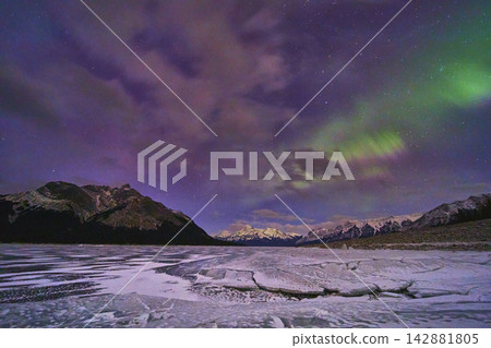 Frozen Lake Northern Lights and Mountain Peaks Under Winter Night Sky Frozen Lake Northern Lights and Mountain Peaks Under Winter Night Sky 142881805