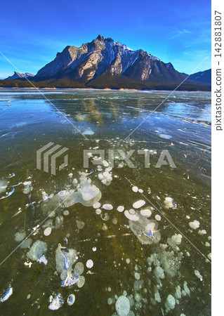 Frozen Lake Methane Bubbles and Majestic Snow Mountain Under Blue Winter Sky 142881807