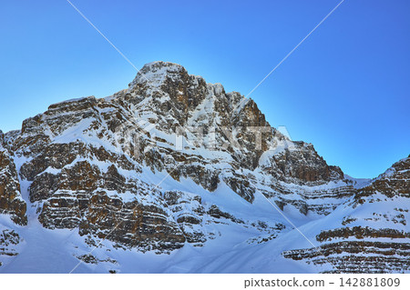 Snow Covered Rocky Mountain Peak Under Clear Blue Winter Sky 142881809