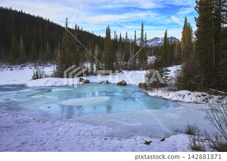 Frozen Pond and Snowy Forest with Mountain Backdrop in Alberta Winter Frozen Pond and Snowy Forest with Mountain Backdrop in Alberta Winter 142881871