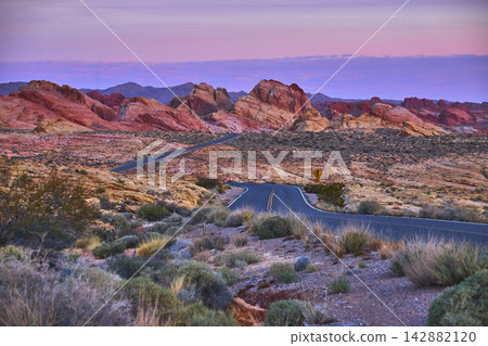 Winding Desert Road at Sunrise with Colorful Sandstone Formations and Open Landscape 142882120