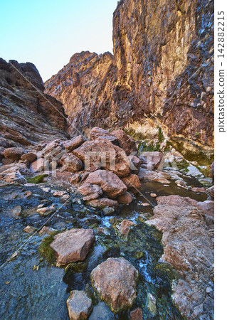 Rocky Canyon Walls Flowing Stream and Boulders at Sunrise in Desert Landscape Rocky Canyon Walls Flowing Stream and Boulders at Sunrise in Desert Landscape 142882215