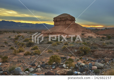 Sandstone Formation Desert Landscape at Sunset with Mountains and Shrubs Sandstone Formation Desert Landscape at Sunset with Mountains and Shrubs 142882237