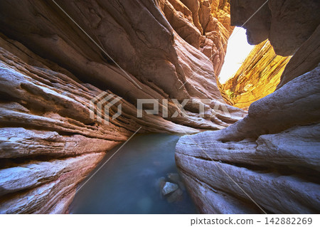 Slot Canyon Pool with Layered Rock Walls and Sunlit Water Reflections Slot Canyon Pool with Layered Rock Walls and Sunlit Water Reflections 142882269