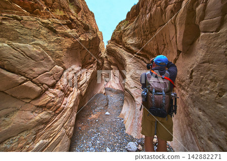 Photographer Exploring Slot Canyon in Nevada with Rugged Rock Walls and Hiking Gear Photographer Exploring Slot Canyon in Nevada with Rugged Rock Walls and Hiking Gear 142882271