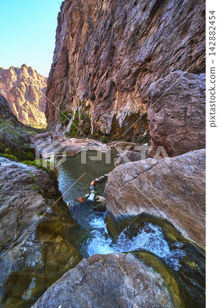 Hot Spring Pool and Waterfall in Rugged Desert Canyon with Hiker Exploring Hot Spring Pool and Waterfall in Rugged Desert Canyon with Hiker Exploring 142882454